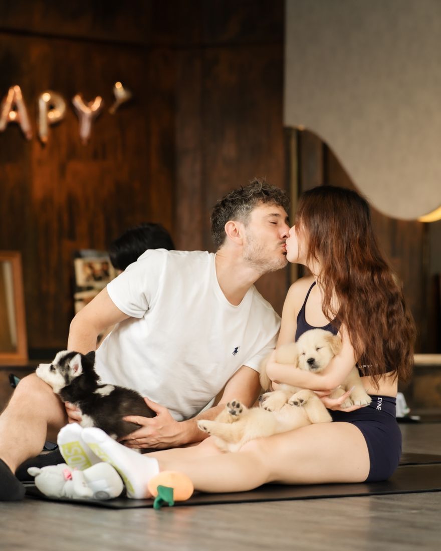 Couple sharing a kiss with puppies on their laps